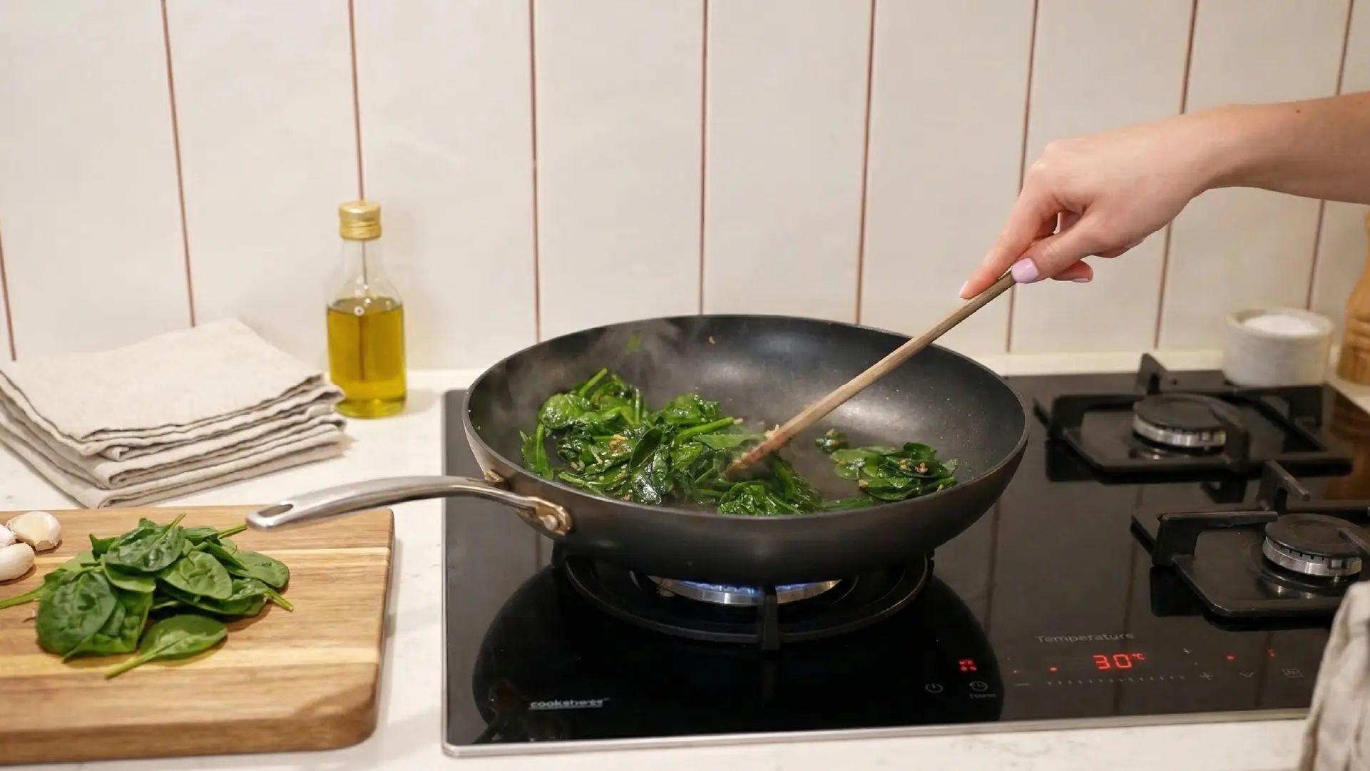Fresh spinach being sautéed in a black skillet on a modern induction stovetop with a wooden spoon.