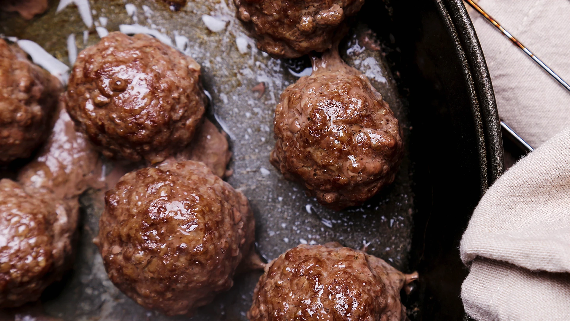 Beef meatballs are being cooked in an oiled frying pan in a kitchen