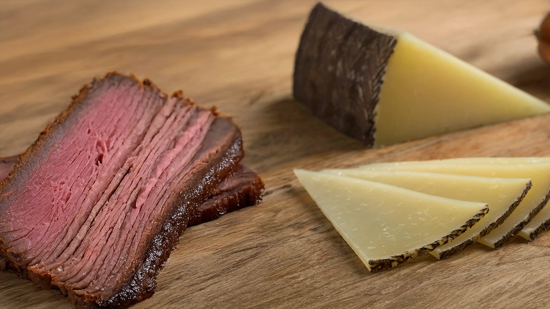A close up shot of Gruyère cheese and pastrami on a wooden surface