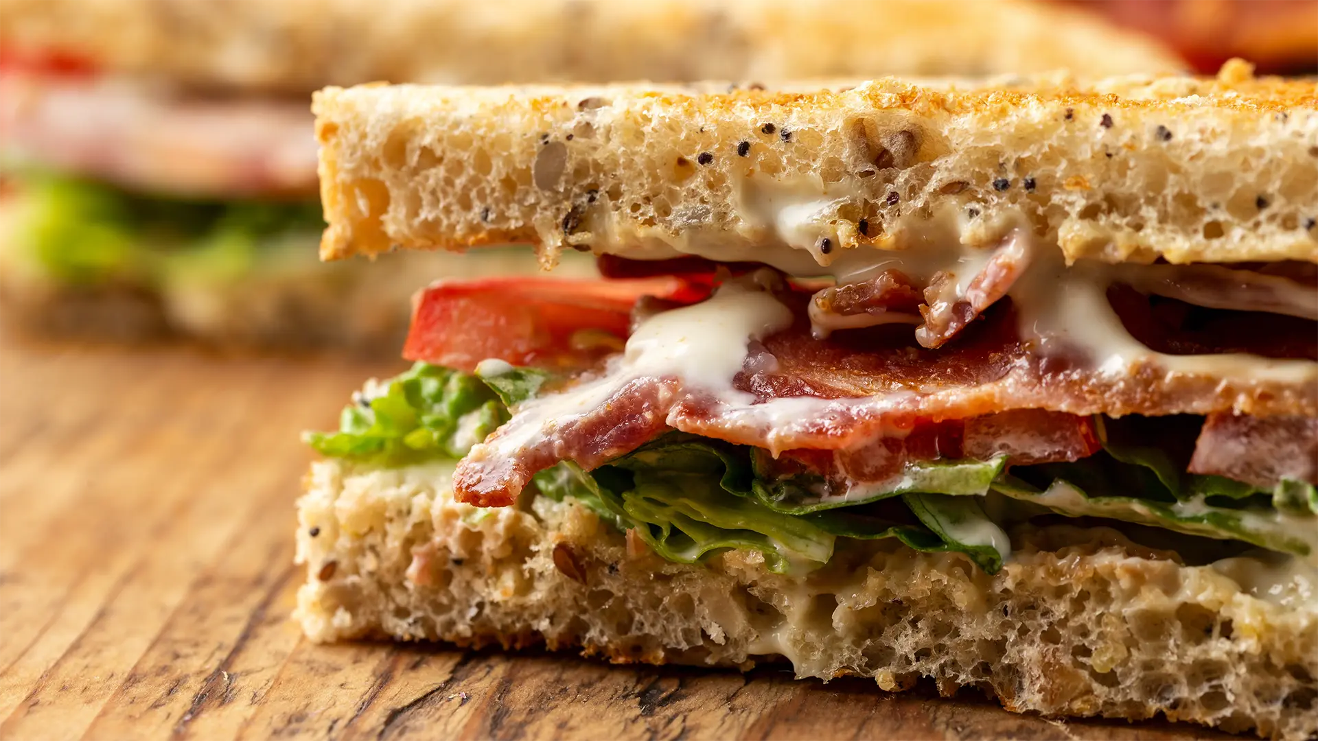 A close up of a BLT sandwich sits on a wooden table. It looks delicious!