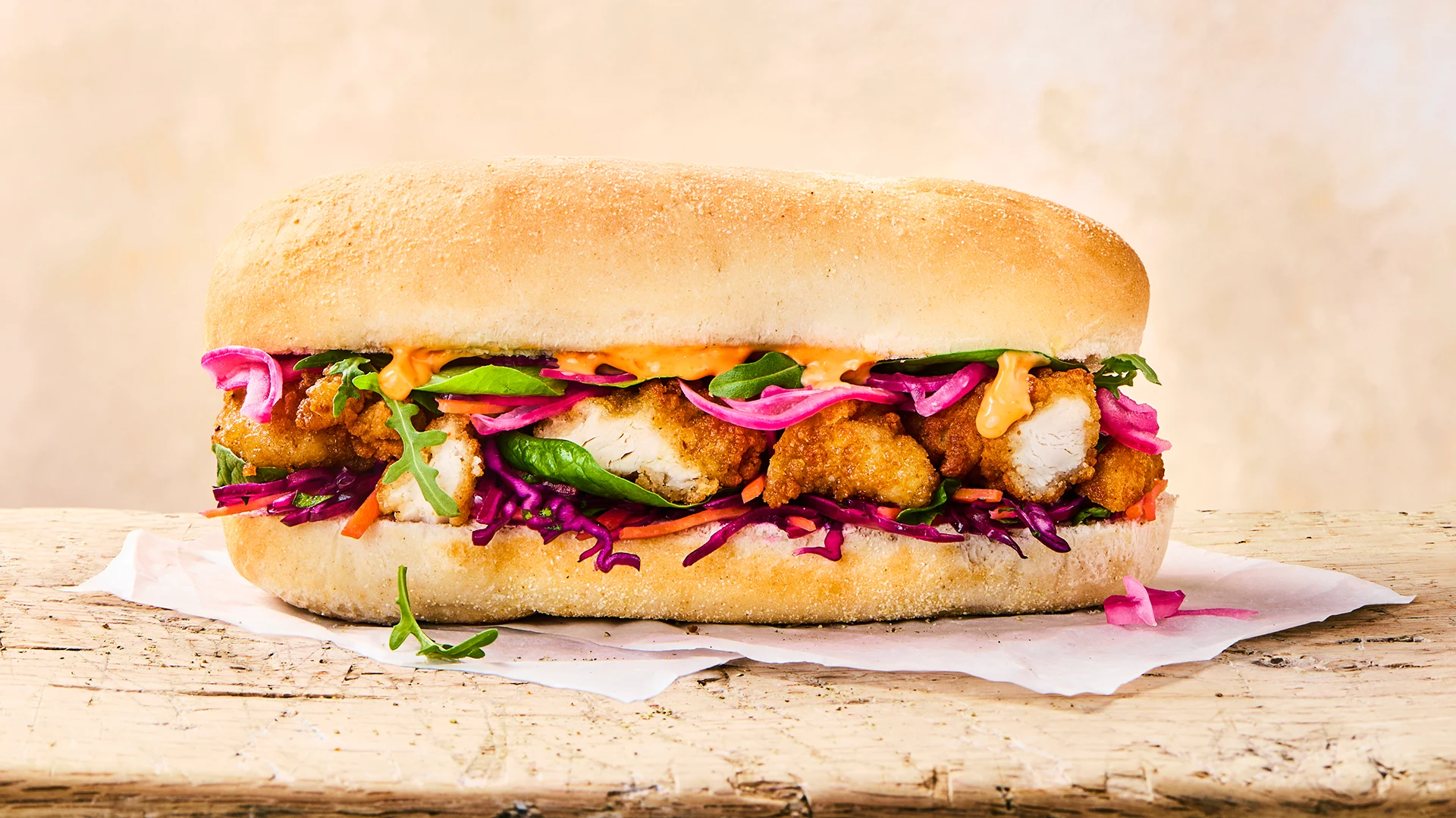 A lovely full Cajun Sub Roll sits on top of some parchment paper on a wooden surface