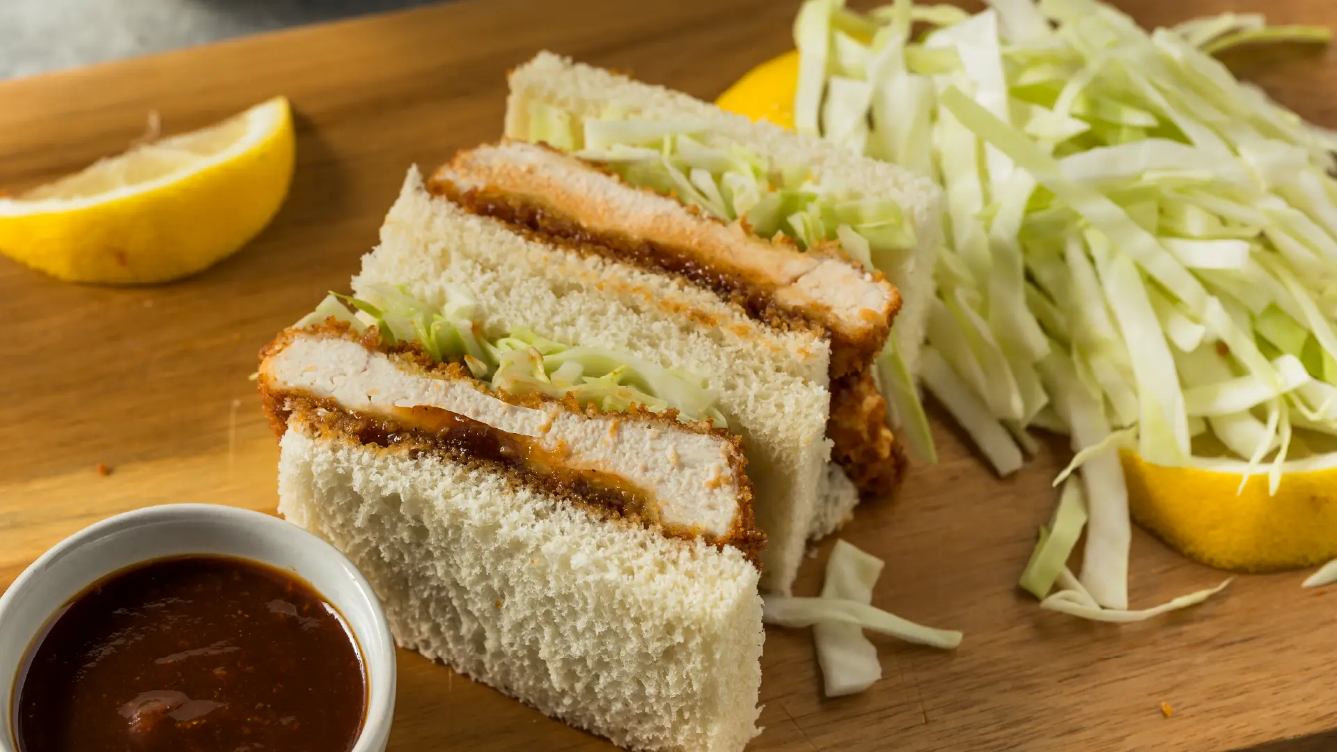 Crispy breaded chicken and shredded cabbage sandwiched between two crustless slices of Hovis Soft White Medium Sliced bread, cut into smaller rectangles.
