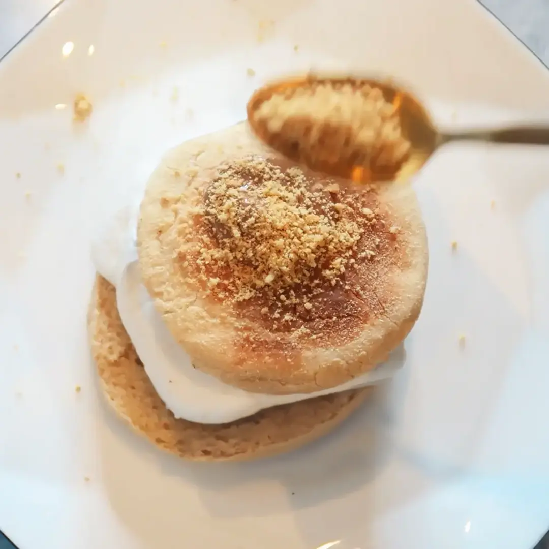 A top-down view of a spoon full of Hovis Digestive Biscuits crumbs being sprinkled on top of the English muffin Smores, on an octagonal plate. 