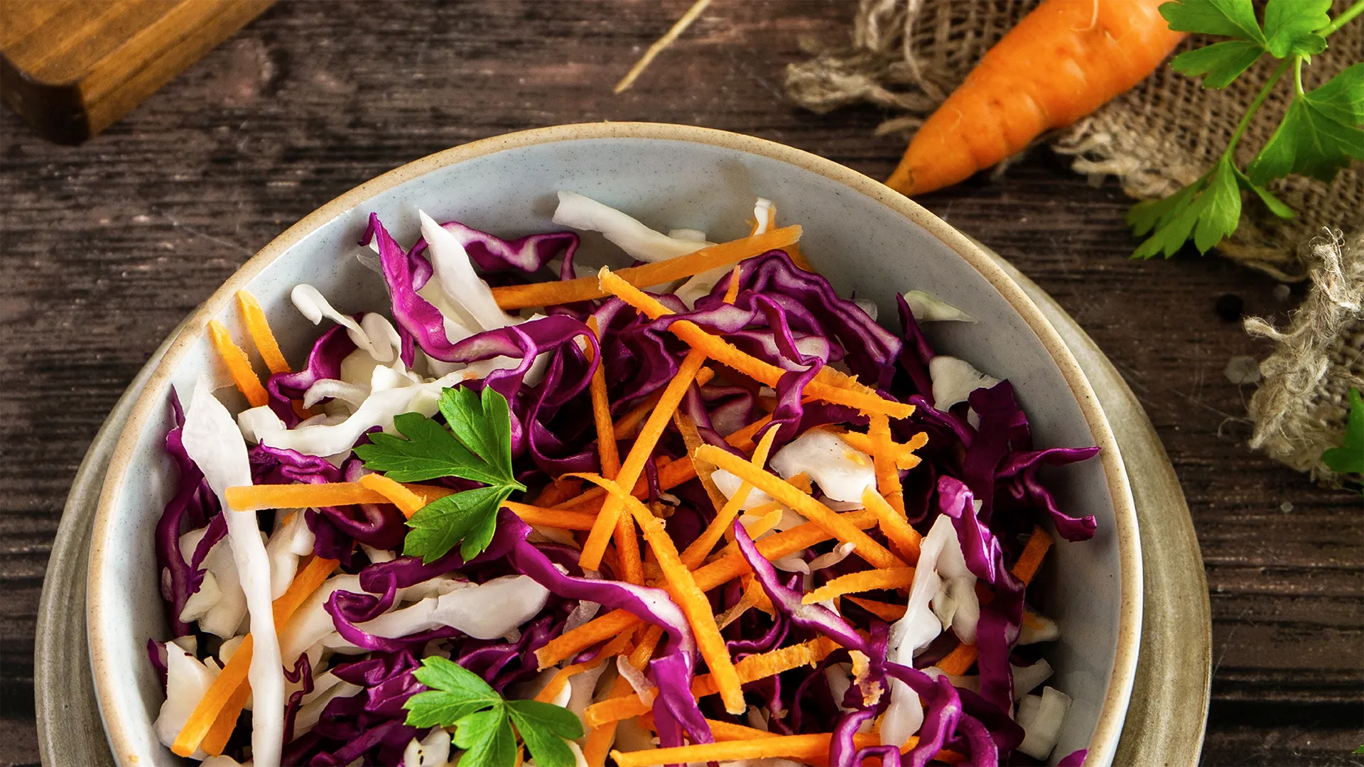 A bowl of slaw on a kitchen counter containing carrot and red cabbage and coriander