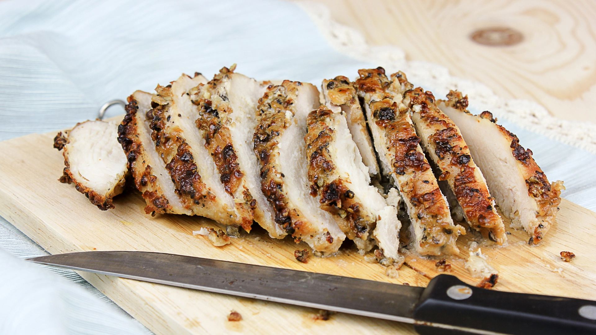 Juicy sliced seasoned chicken breasts on a wooden chopping board. A sharp knife resting on the side.