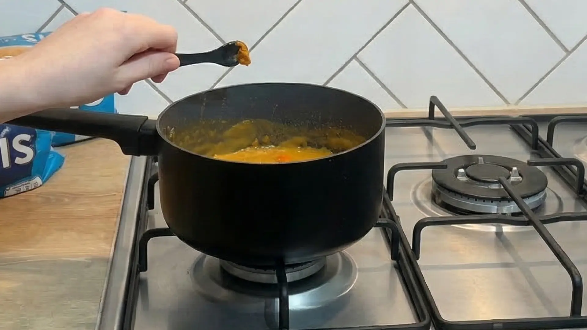 A large saucepan with orange sauce is being cooked on a hob.