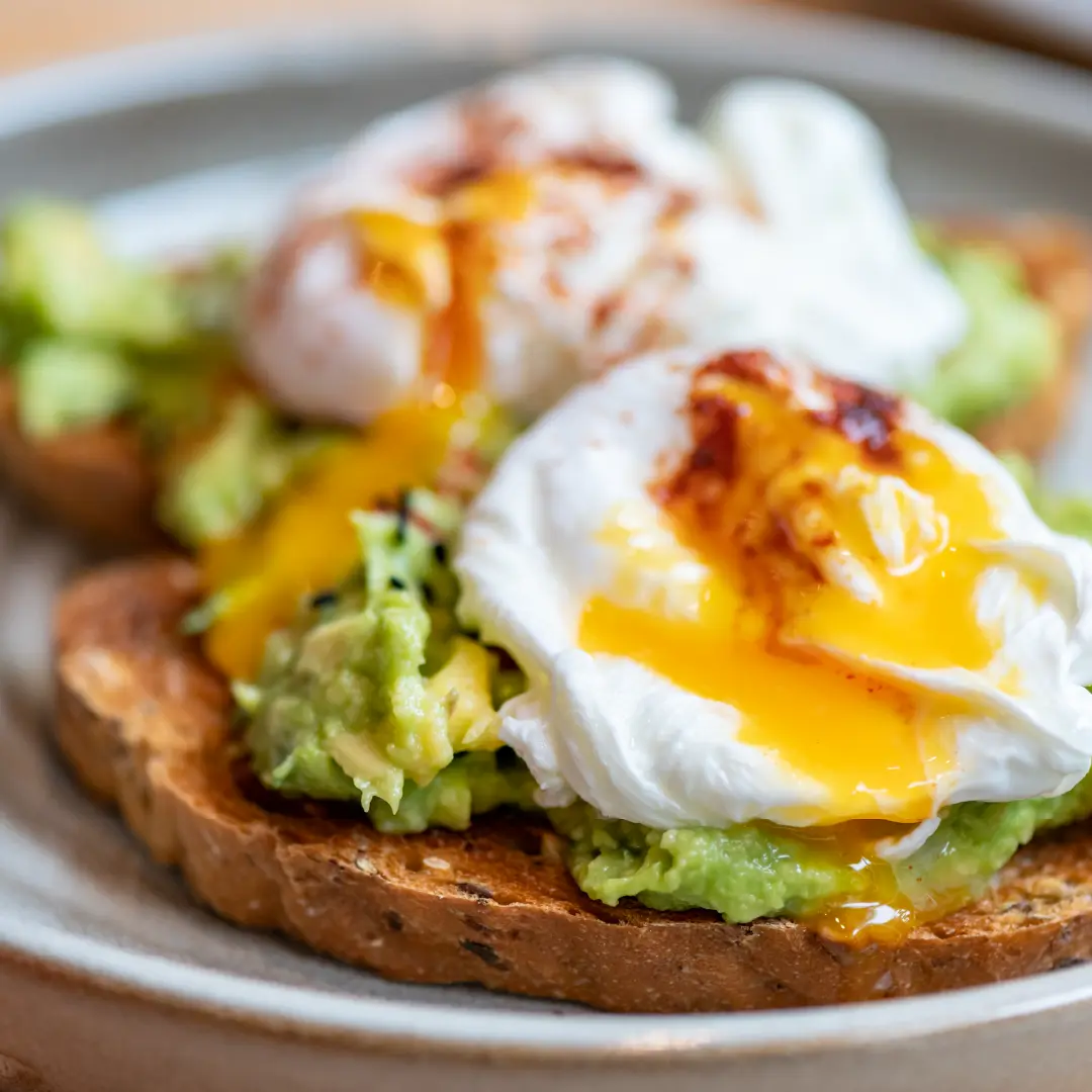 Two slices Hovis Seeded Half Cob bread, slightly toasted, topped with mashed avocado, a poached egg, and a drizzle of crispy chili oil.