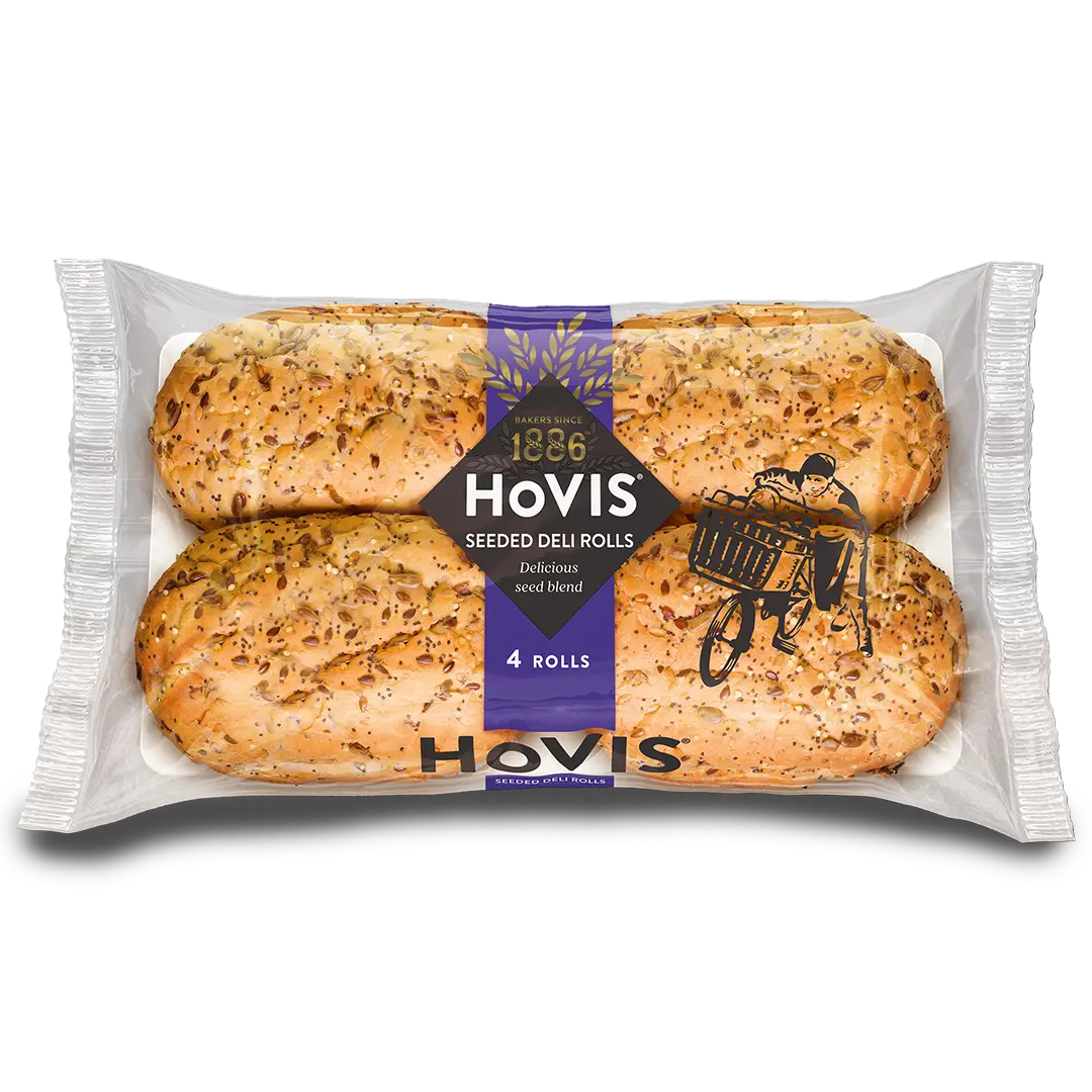 Four Hovis Seeded Deli Rolls are in a rectangular, transparent package. In the middle, a purple strip with Hovis' logo and the year 1886 on top.