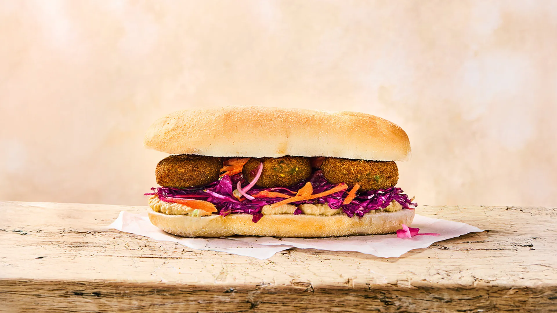 A full falafel, hummus and slaw sub sitting on parchment paper on a wooden surface