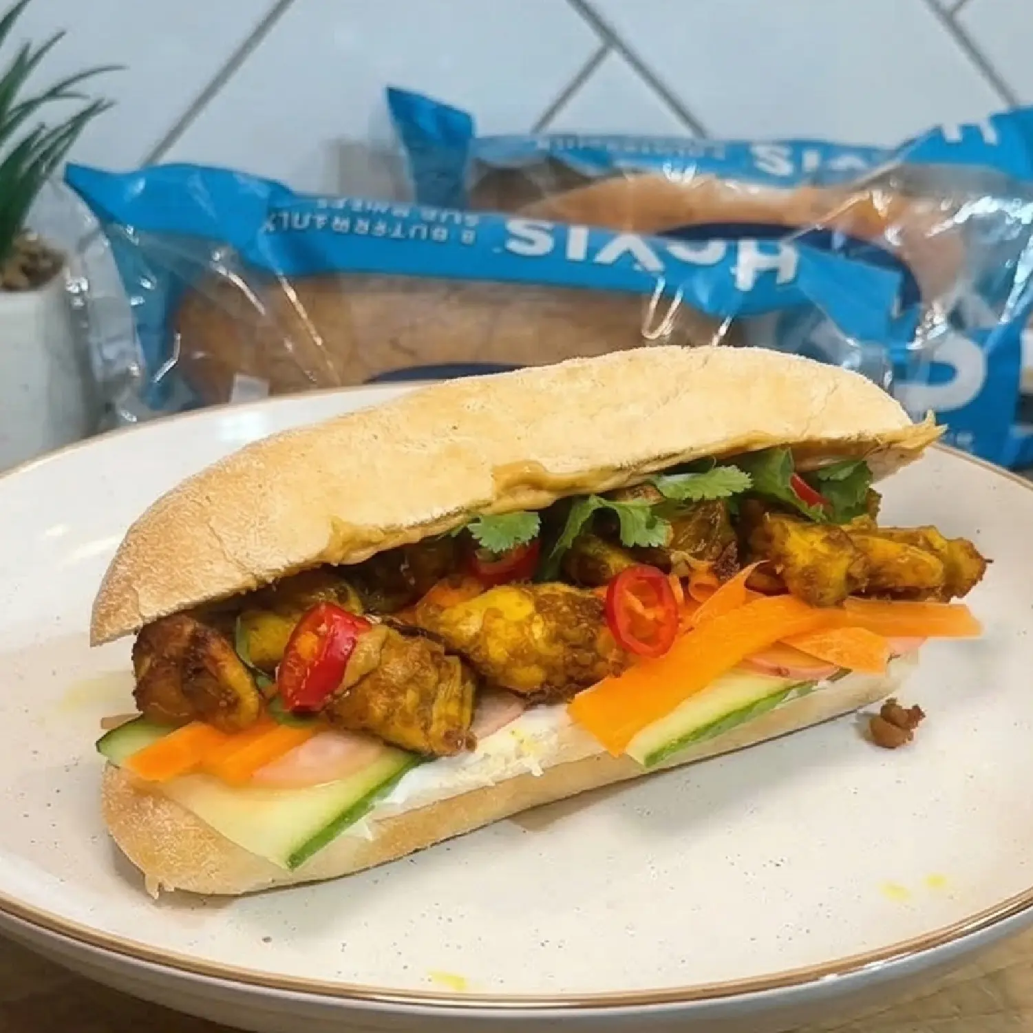 A plated Hovis Buttermilk Sub Roll, sliced in half and filled with satay chicken, pickled radish and carrots and garnished with coriander. 