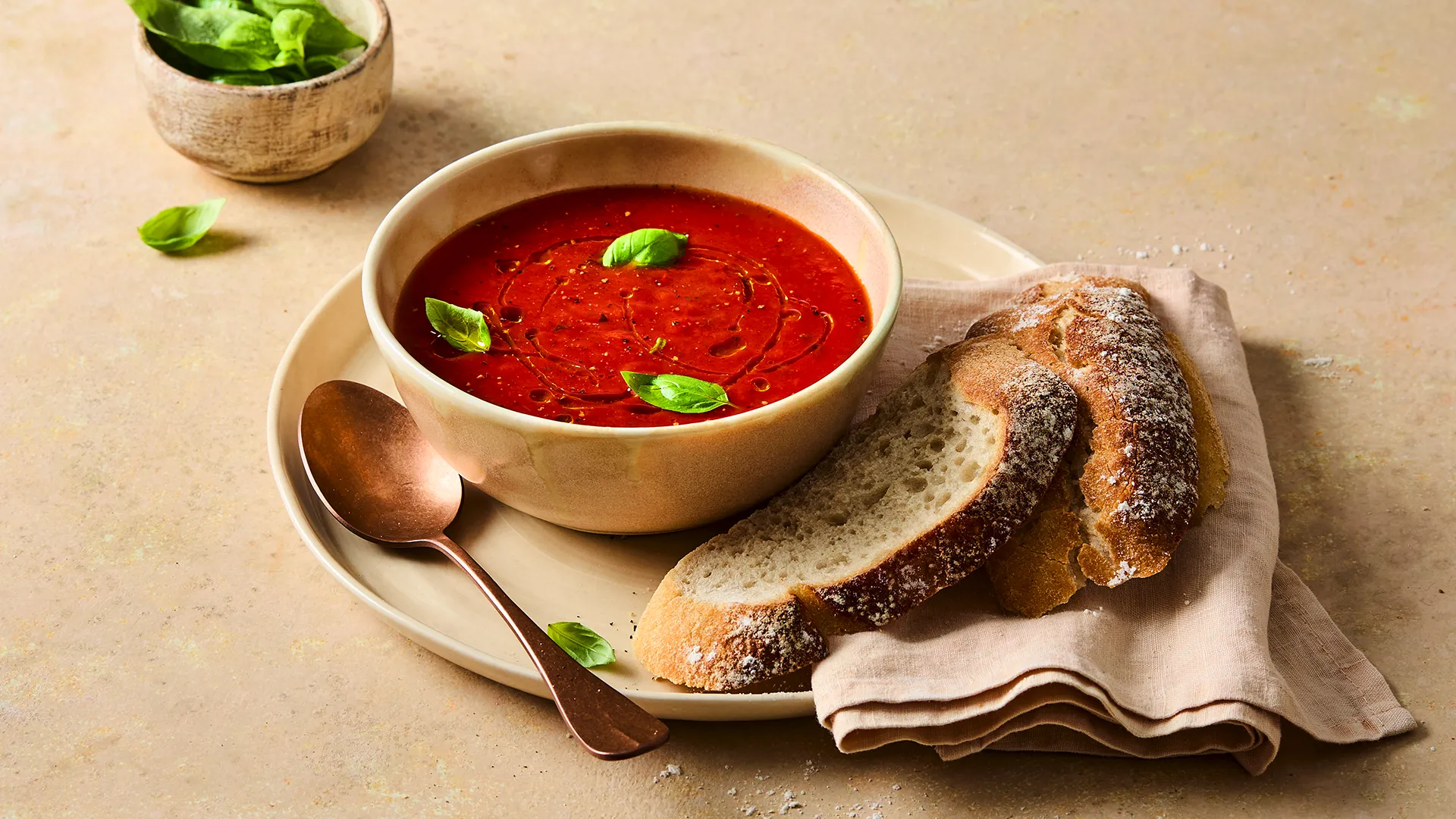 A tomato and basil soup sits on a cream plate with 2 slices of Hovis Sourdough next to it. 