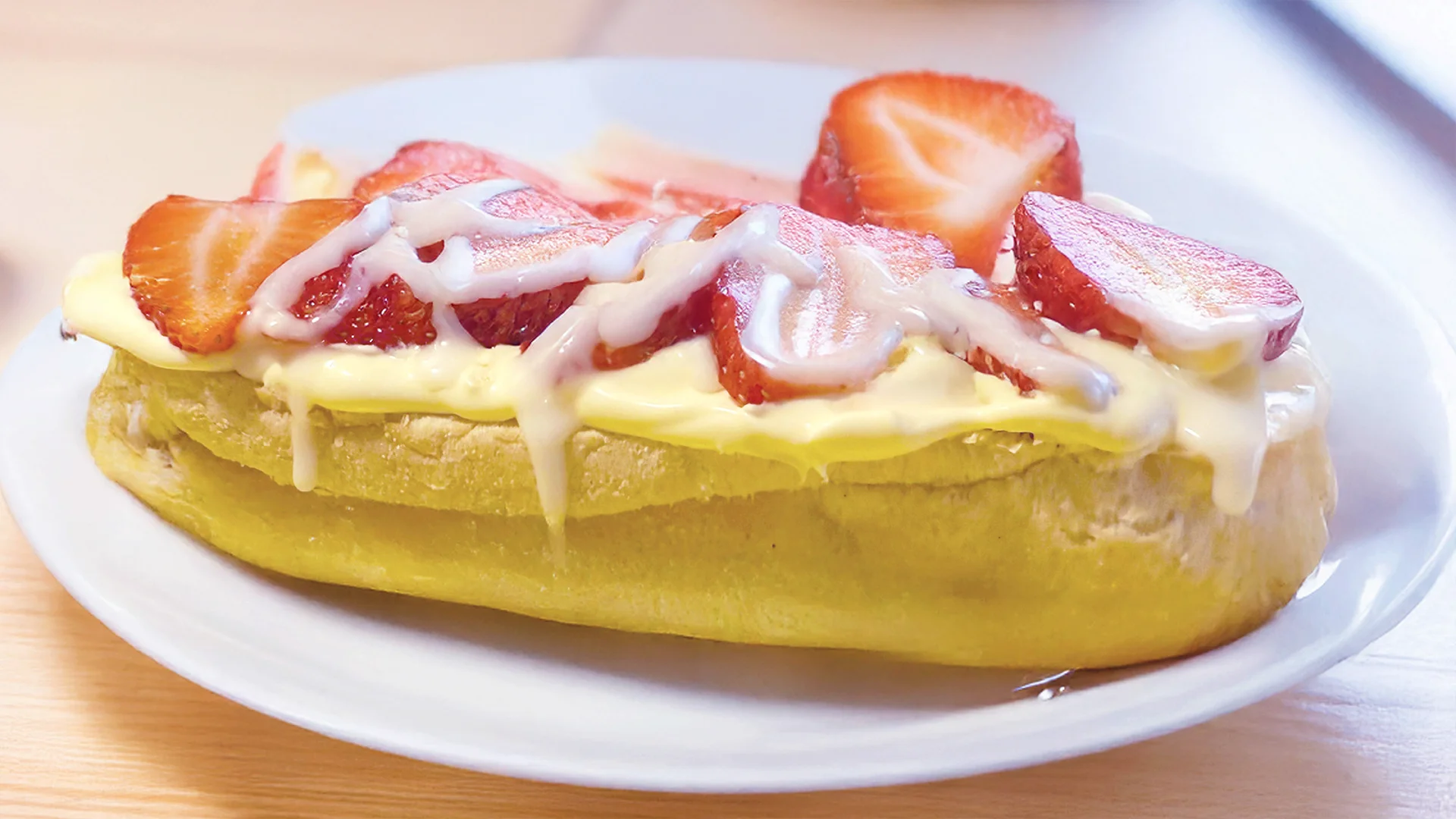 A half a sub roll on a white plate topped with clotted cream and strawberries