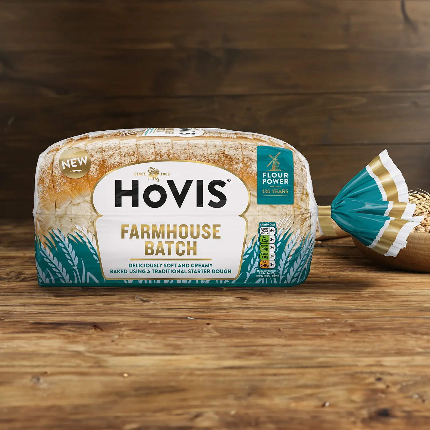 Hovis Farmhouse Batch on a wooden table, with a bowl of wheat grains, a wooden scoop, and dried wheat in the background.