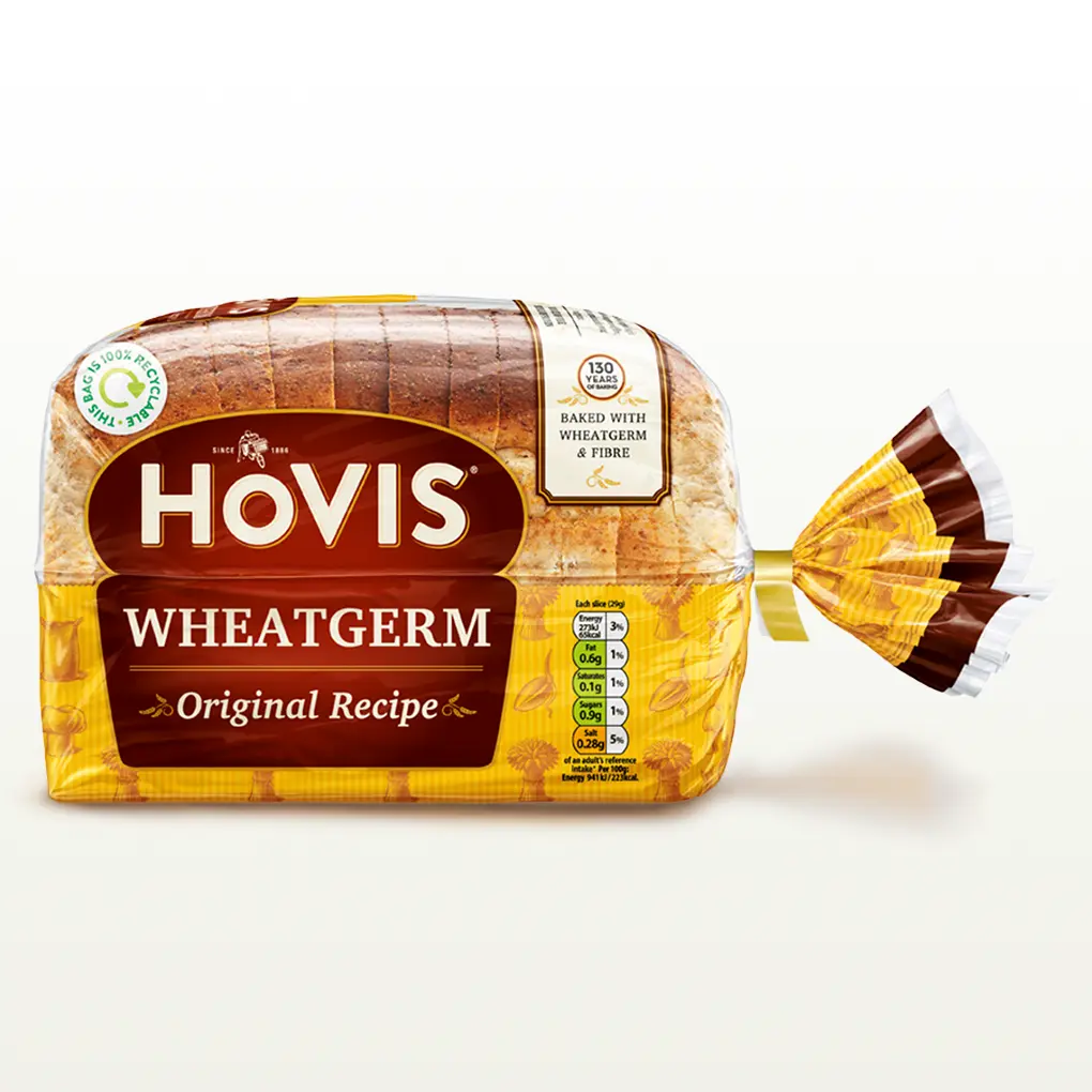 Hovis Wheatgerm 400g bread on a white backdrop with a subtle shadow. The packaging is half transparent and half yellow, decorated with images of wheatgerm, a chefs hat, flour and wheats.