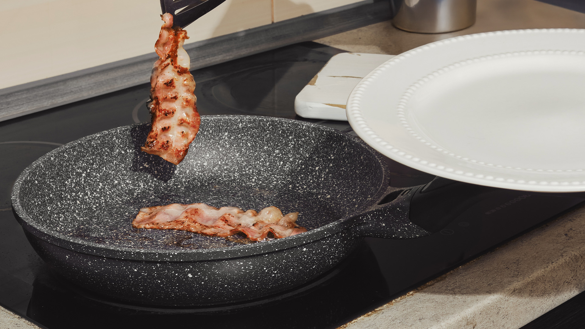 A close-up of bacon frying on an oiled pan.