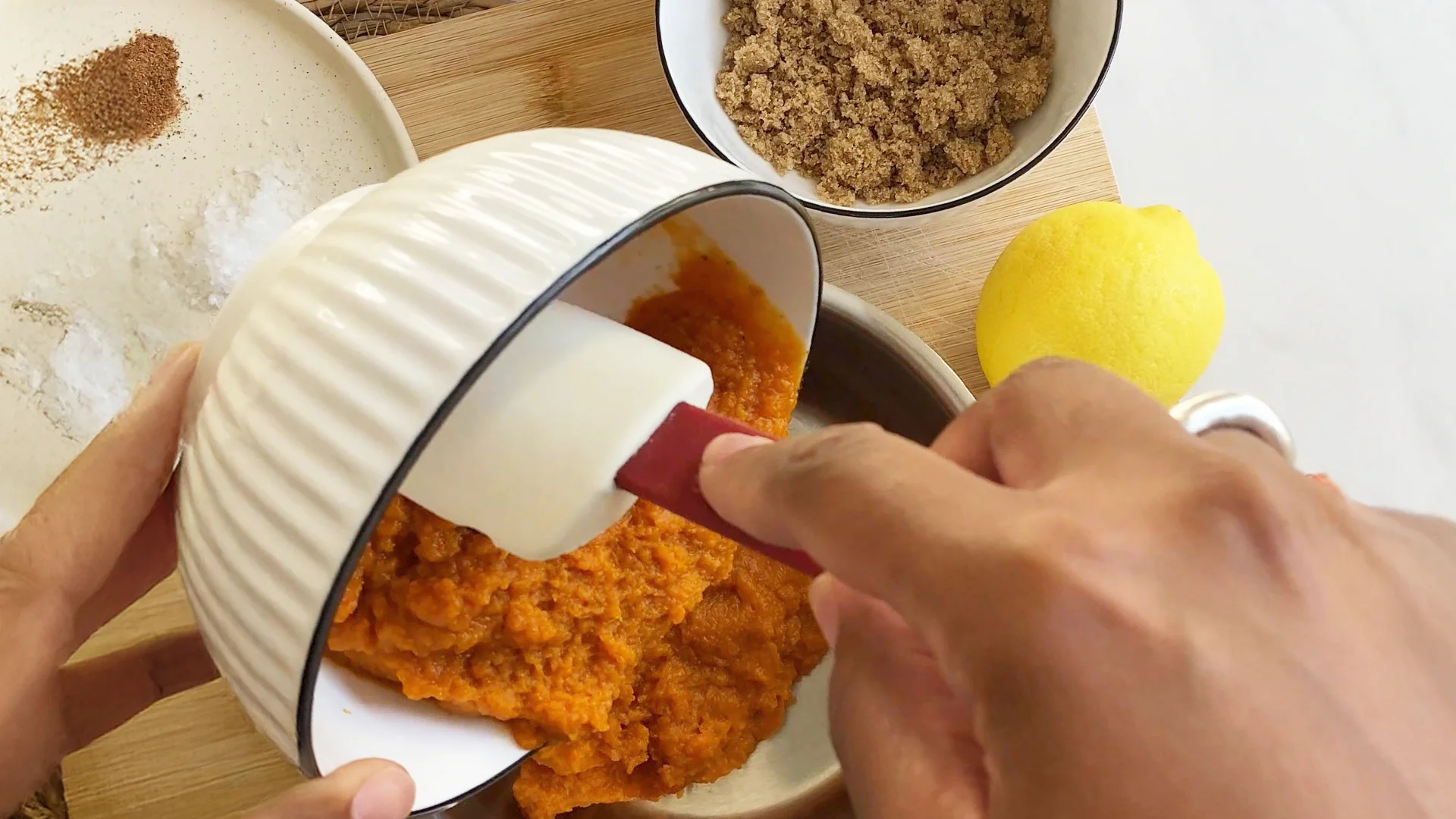 Pumpkin puree is being poured into another bowel with the rest of the ingredients nearby, such as lemon, sugar and nutmeg