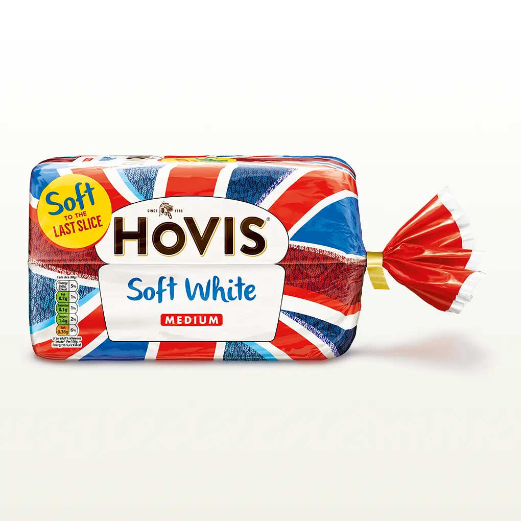 Hovis Soft White Medium Sliced bread on a white backdrop with a subtle shadow. The packaging features a Union Jack pattern and a yellow label reading 'Soft to the Last Slice.'
