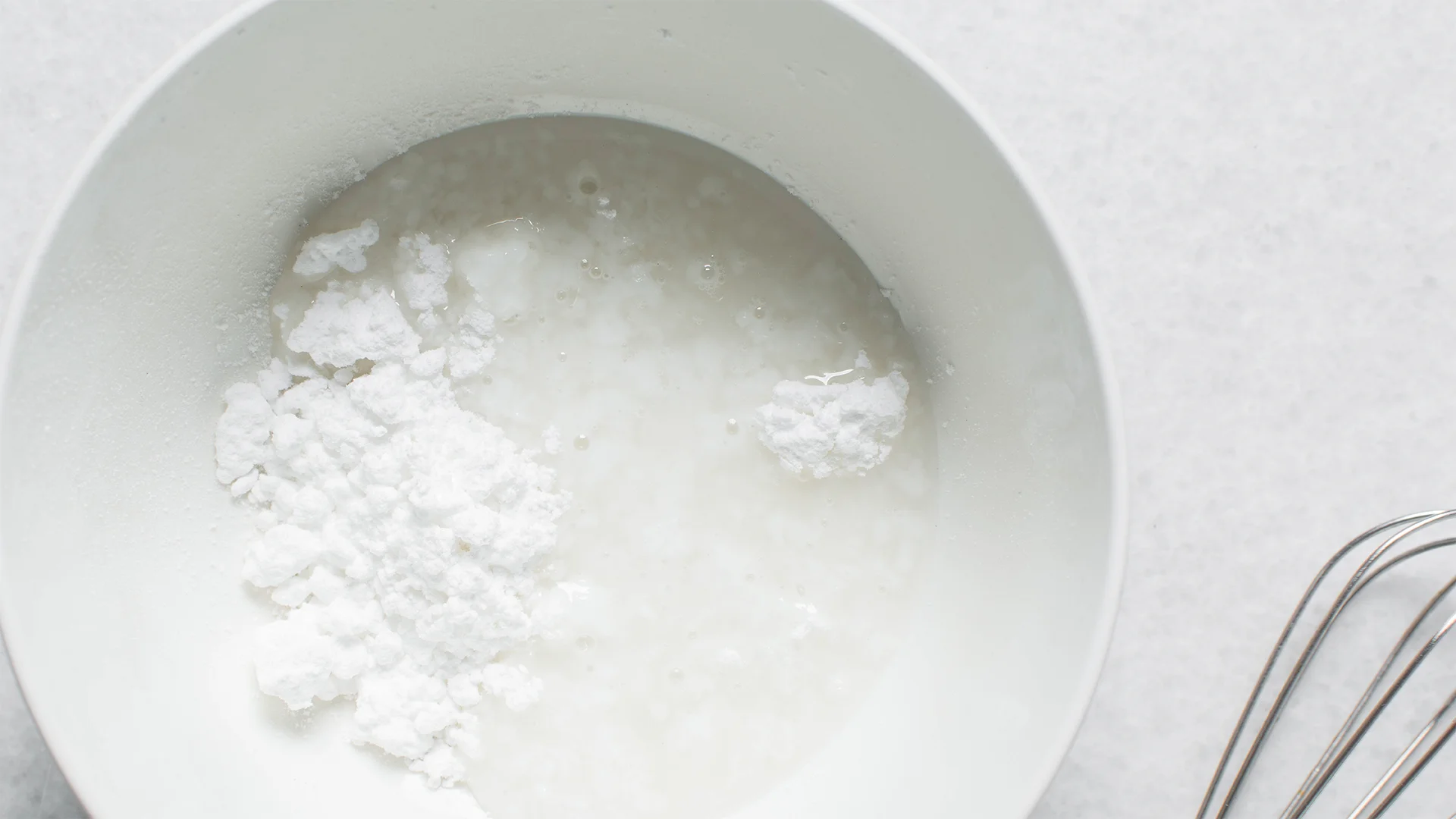 A white bowl with icing sugar and water inside ready to be mixed with a whisk into icing