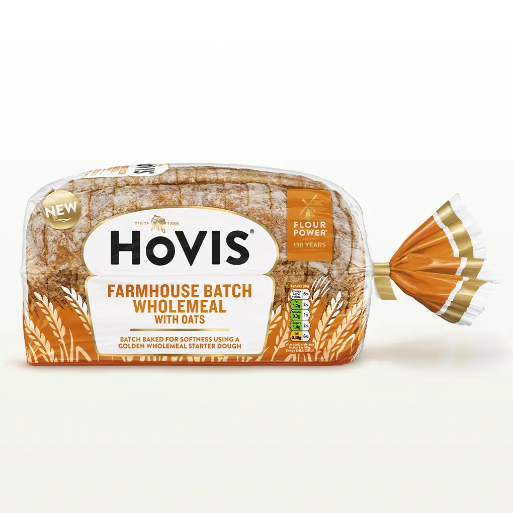 Hovis Farmhouse Batch Wholemeal bread on a white backdrop with a subtle shadow. The packaging is half transparent and orange, decorated with wheats.