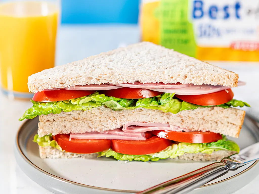 A sandwich made with Hovis best of both loaf, tomatoes, ham, lettuce and butter sits on a plate in a kitchen