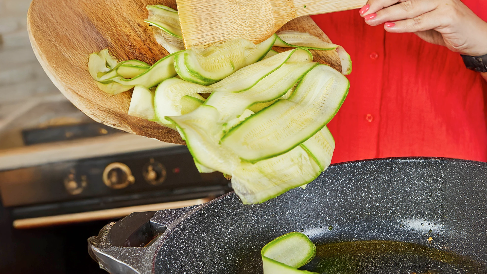Someone is putting courgette ribbons into an oiled frying pan for cooking 