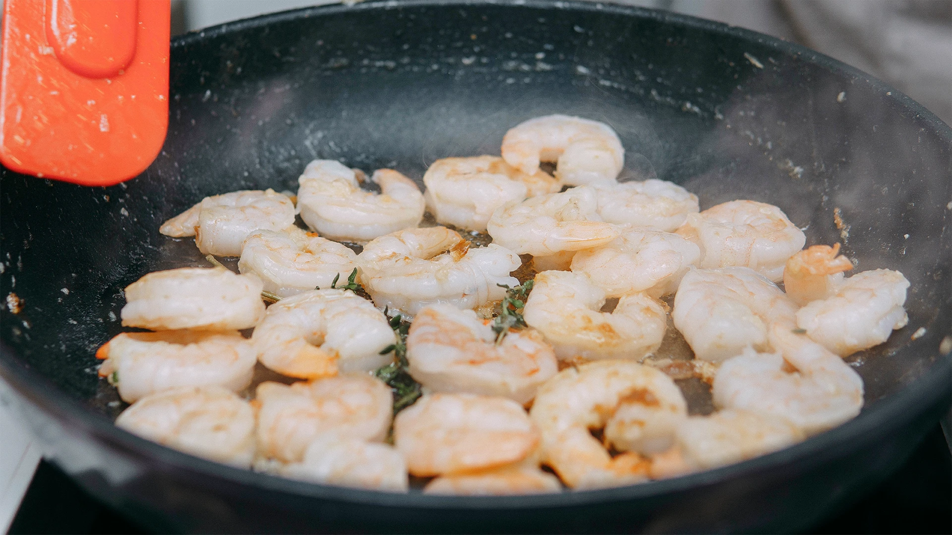 Prawns are cooking on a black frying pan with a red spatula waiting to stir 
