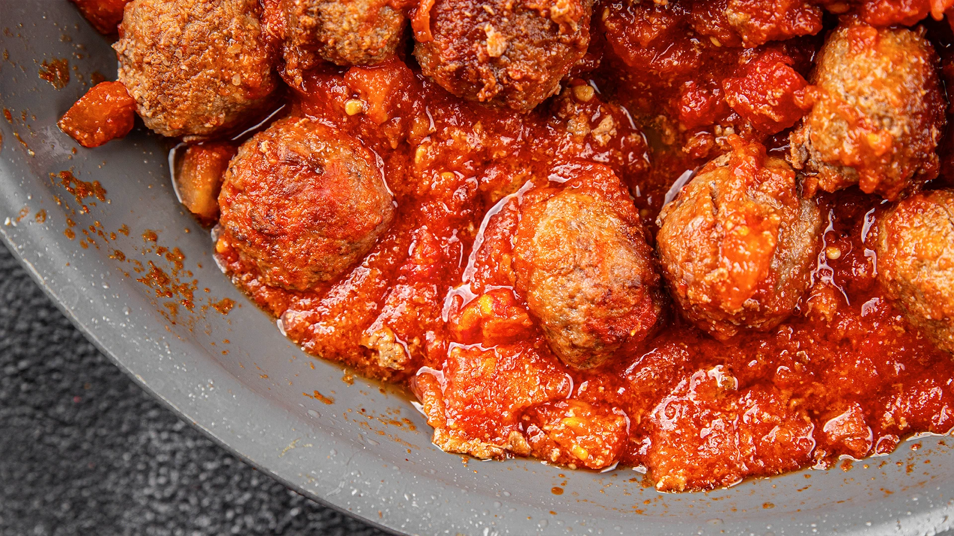 Beef meatballs cook in a pan with chopped tomatoes