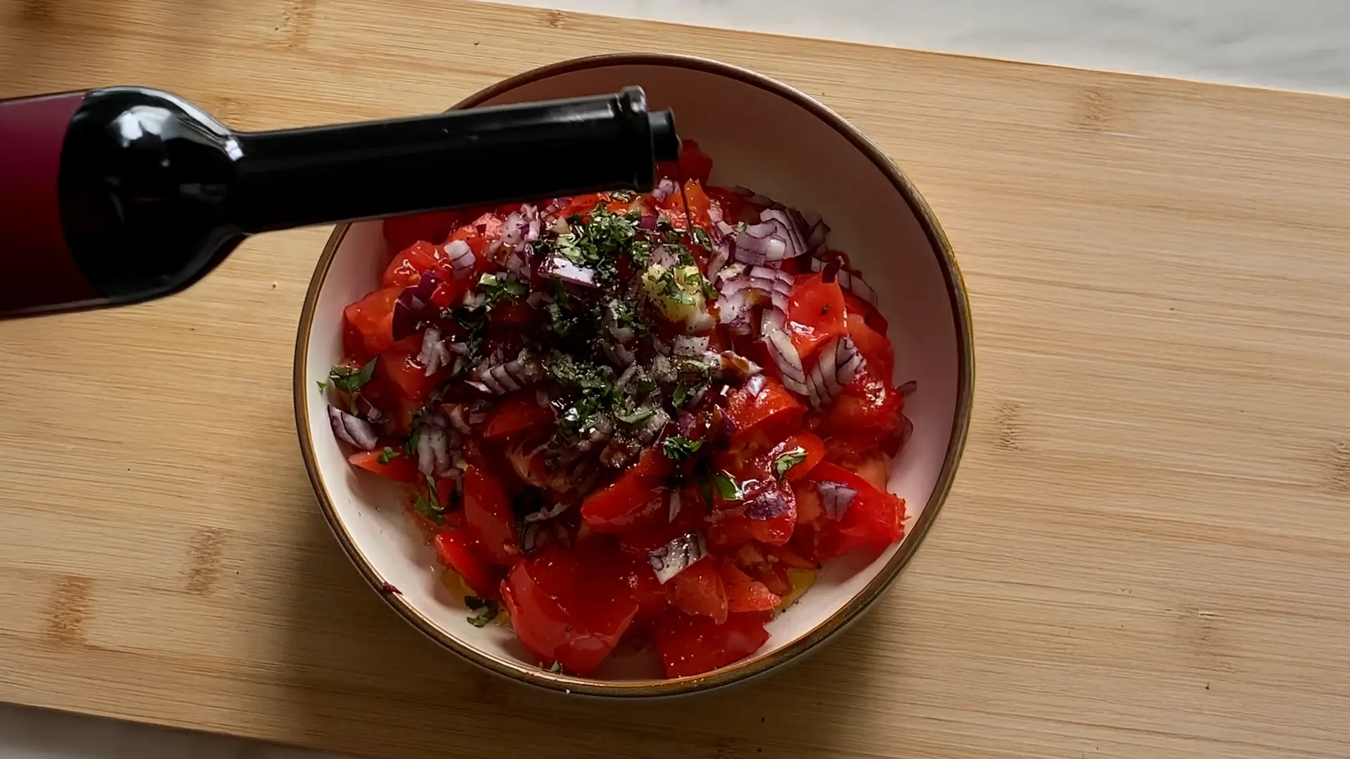 A bowl of diced tomatoes, onions and basil. In the background, some vined tomatoes, halved red onions and herbs.