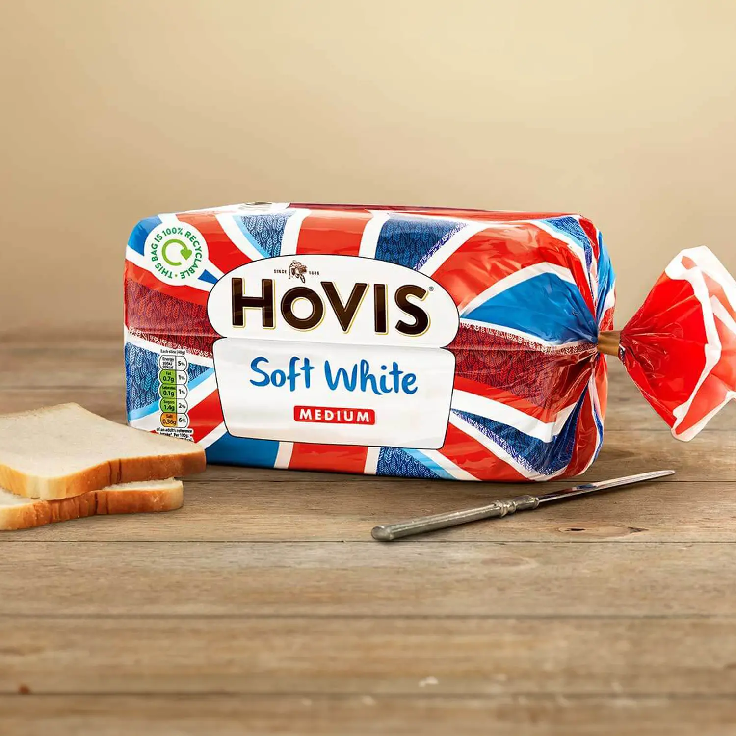 Hovis Soft White Medium Sliced bread on a wooden table, with two stacked slices on the left and a metal butter knife on the right.