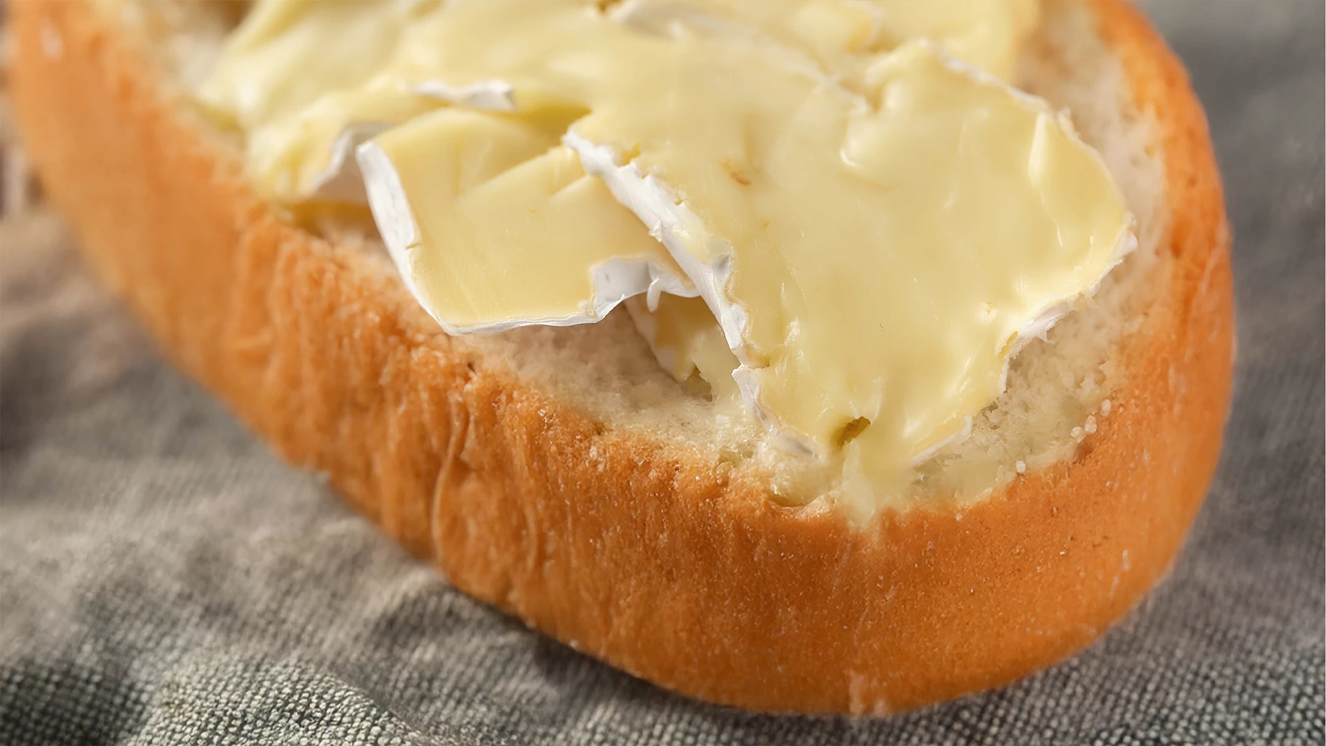 a close up of melted brie cheese on the bottom half of a cheese and herb sub roll 