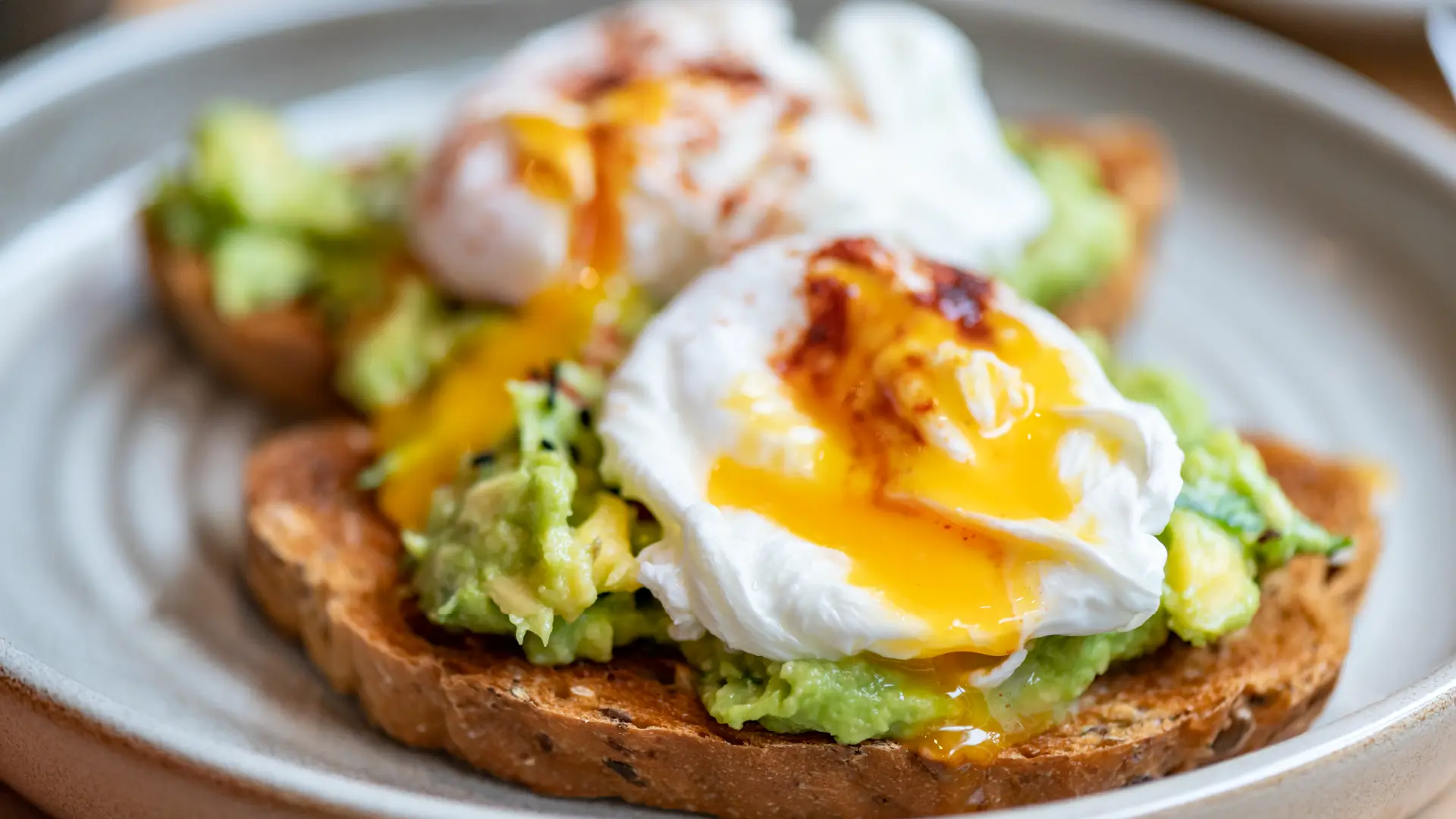 Two slices Hovis Seeded Half Cob bread, slightly toasted, topped with mashed avocado, a poached egg, and a drizzle of crispy chili oil.