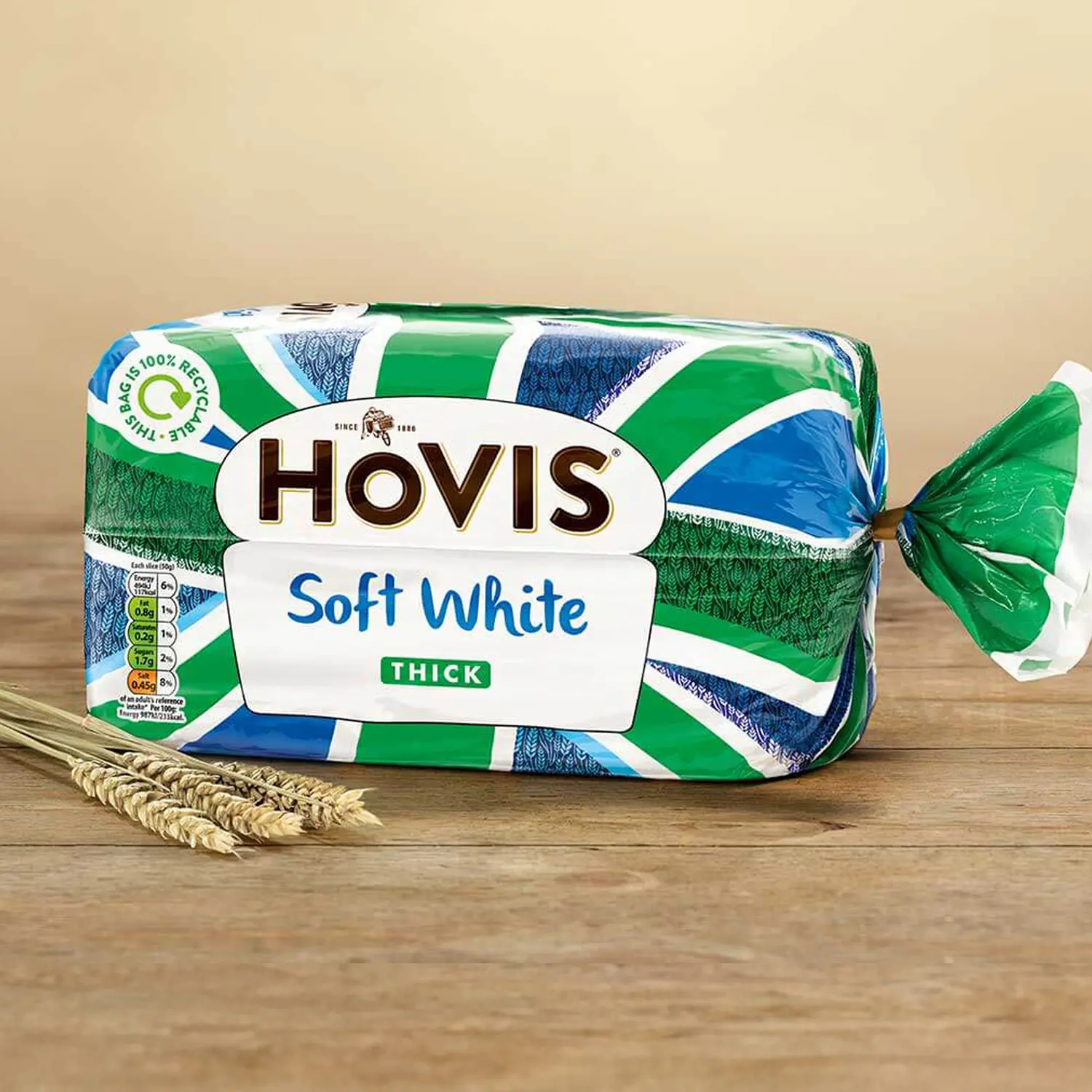 Hovis Soft White Thick Sliced bread against a beige background on a wooden table, with some dried wheat stalks on the left.