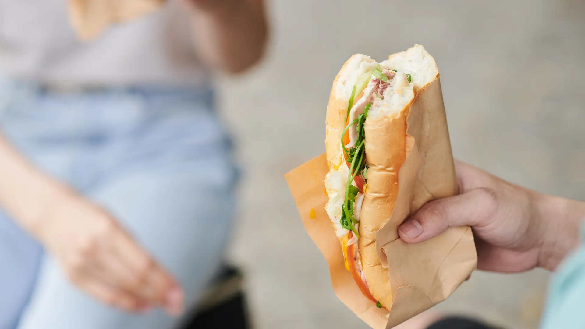 Someone is holding a sub roll with ham and rocket