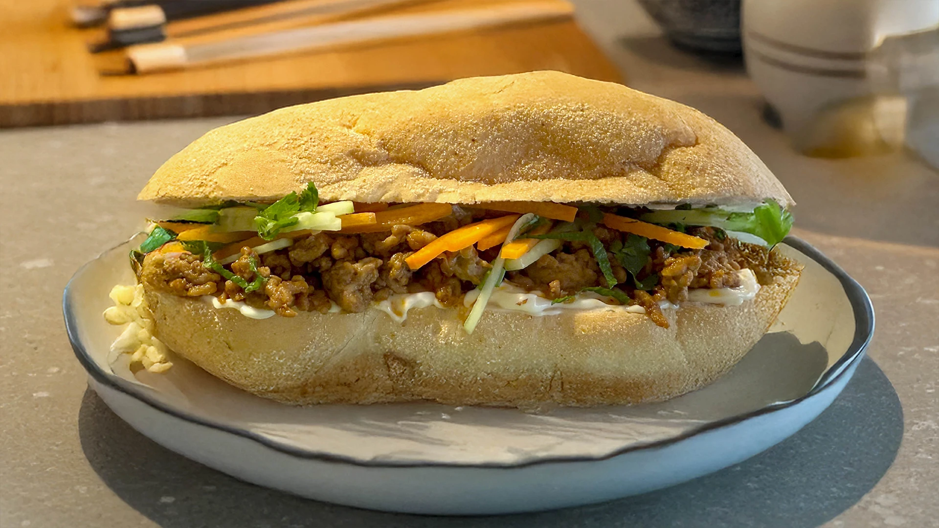 A lovely full Asian Spiced Pork Sub sits on a white plate on a kitchen counter