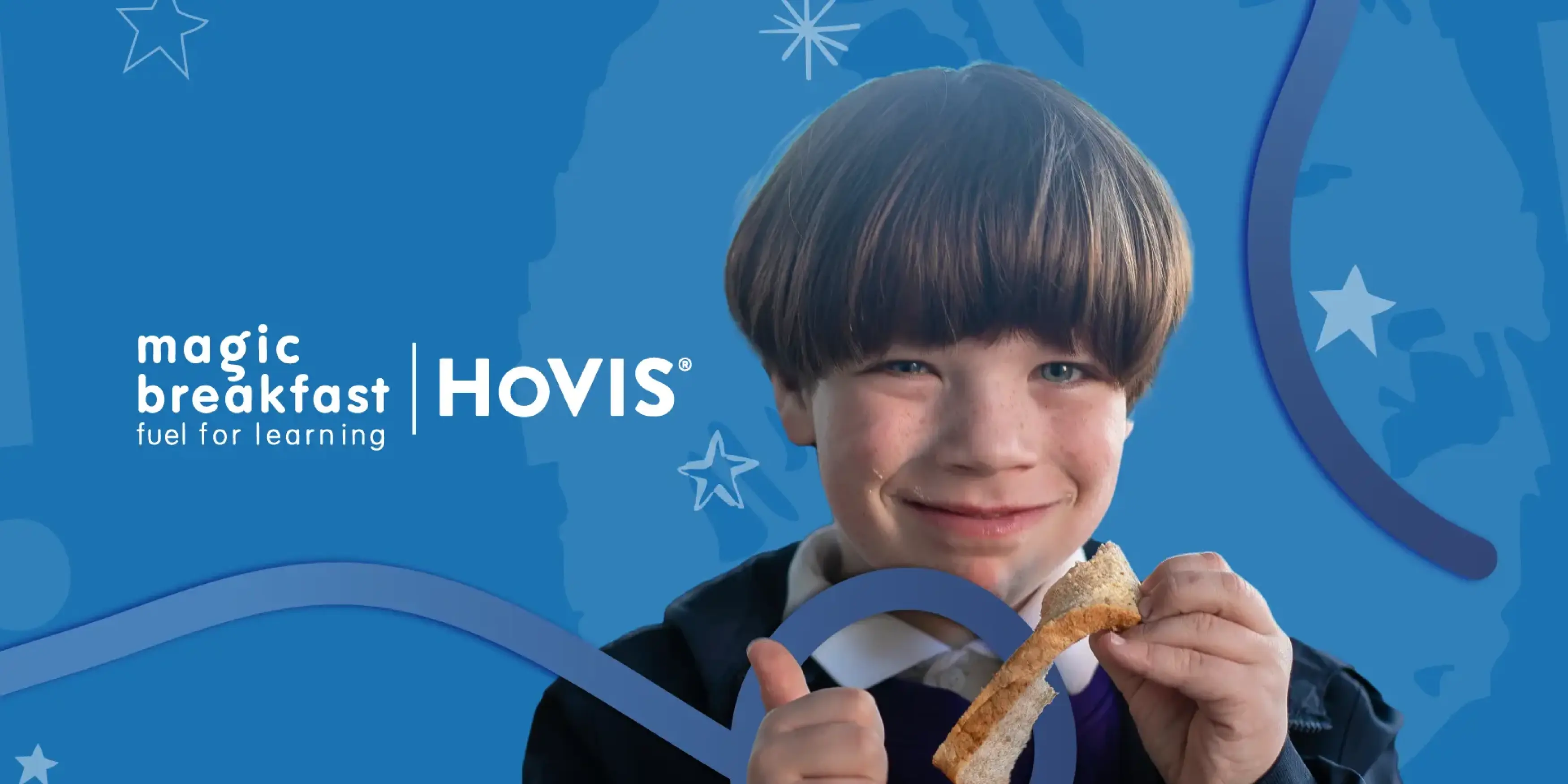 A young child with brown hair in a bowl cut smiles broadly at the camera while holding a piece of toast. The child is giving a thumbs-up with their other hand. They are wearing a school uniform consisting of a white collared shirt under a purple jumper and a dark jacket.