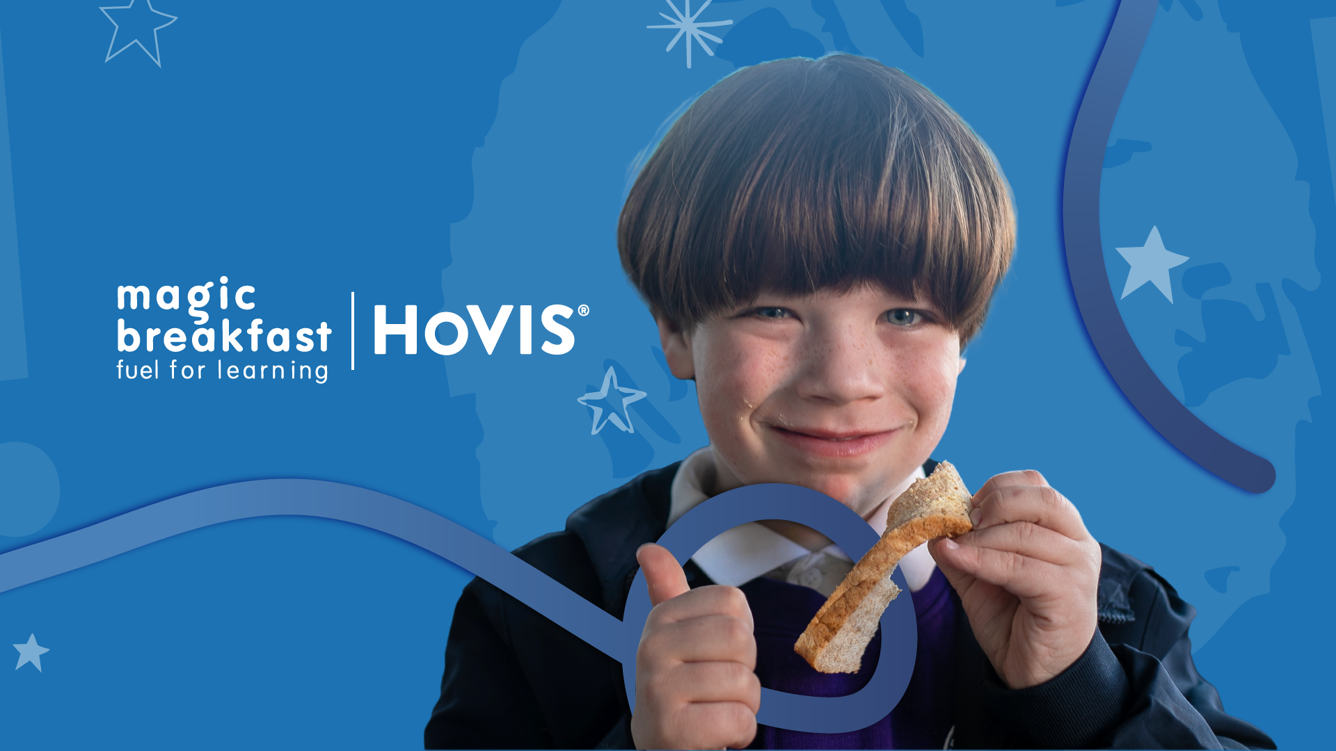 A young child with brown hair in a bowl cut smiles broadly at the camera while holding a piece of toast. The child is giving a thumbs-up with their other hand. They are wearing a school uniform consisting of a white collared shirt under a purple jumper and a dark jacket.