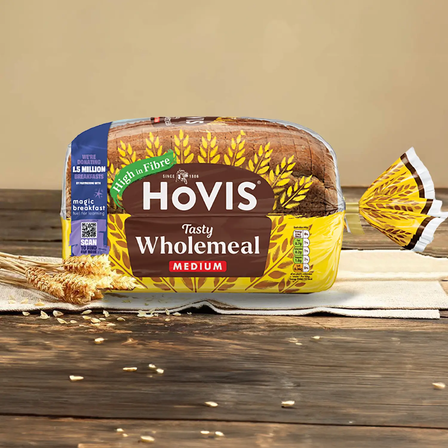 Hovis Tasty Wholemeal Medium Sliced bread on napkins against a light beige background atop a wooden table, surrounded by dried wheat.