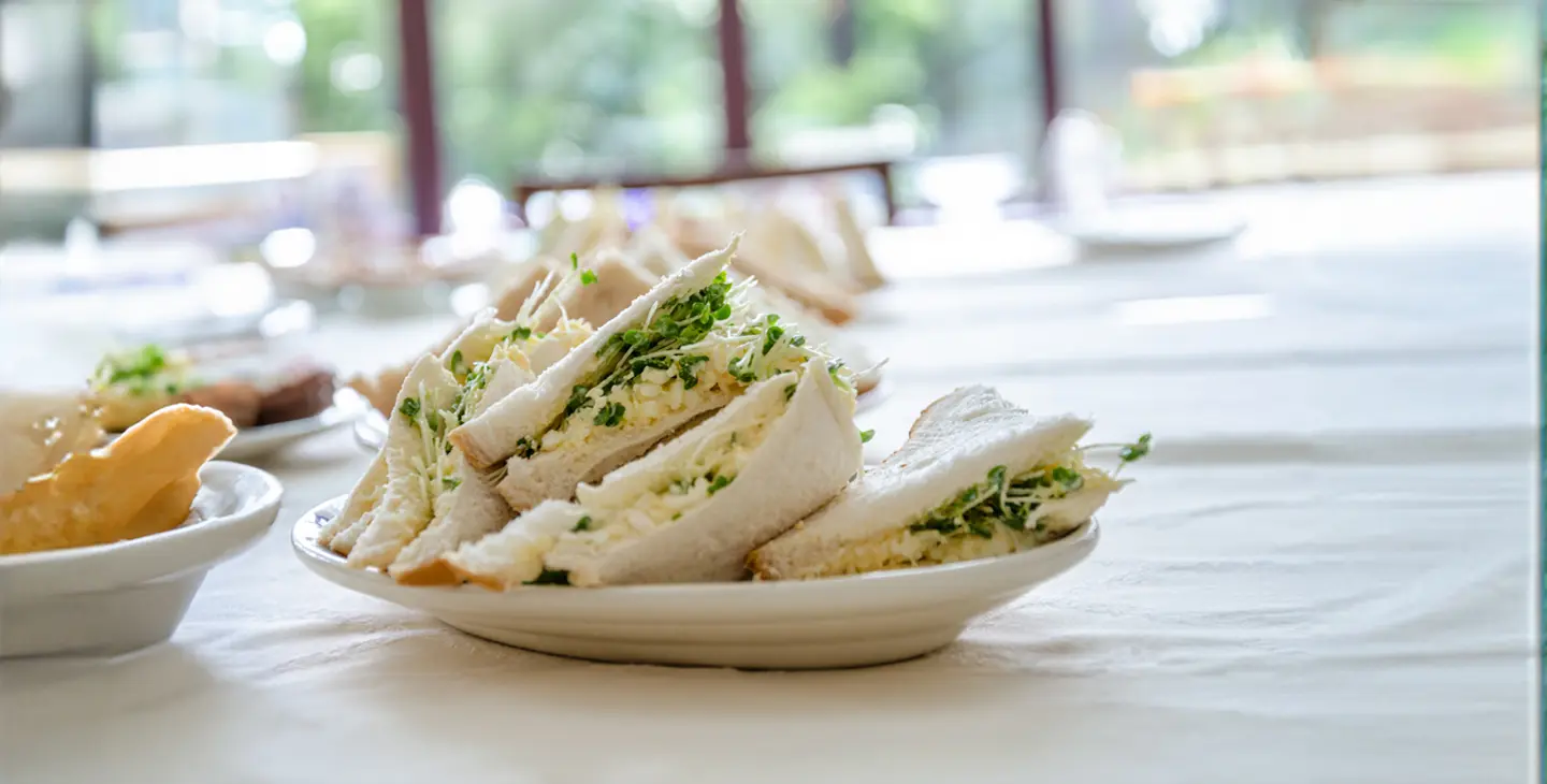 A plate of egg and cress sandwiches sits on a white plate in a light kitchen. They are cut and half and look delicious!