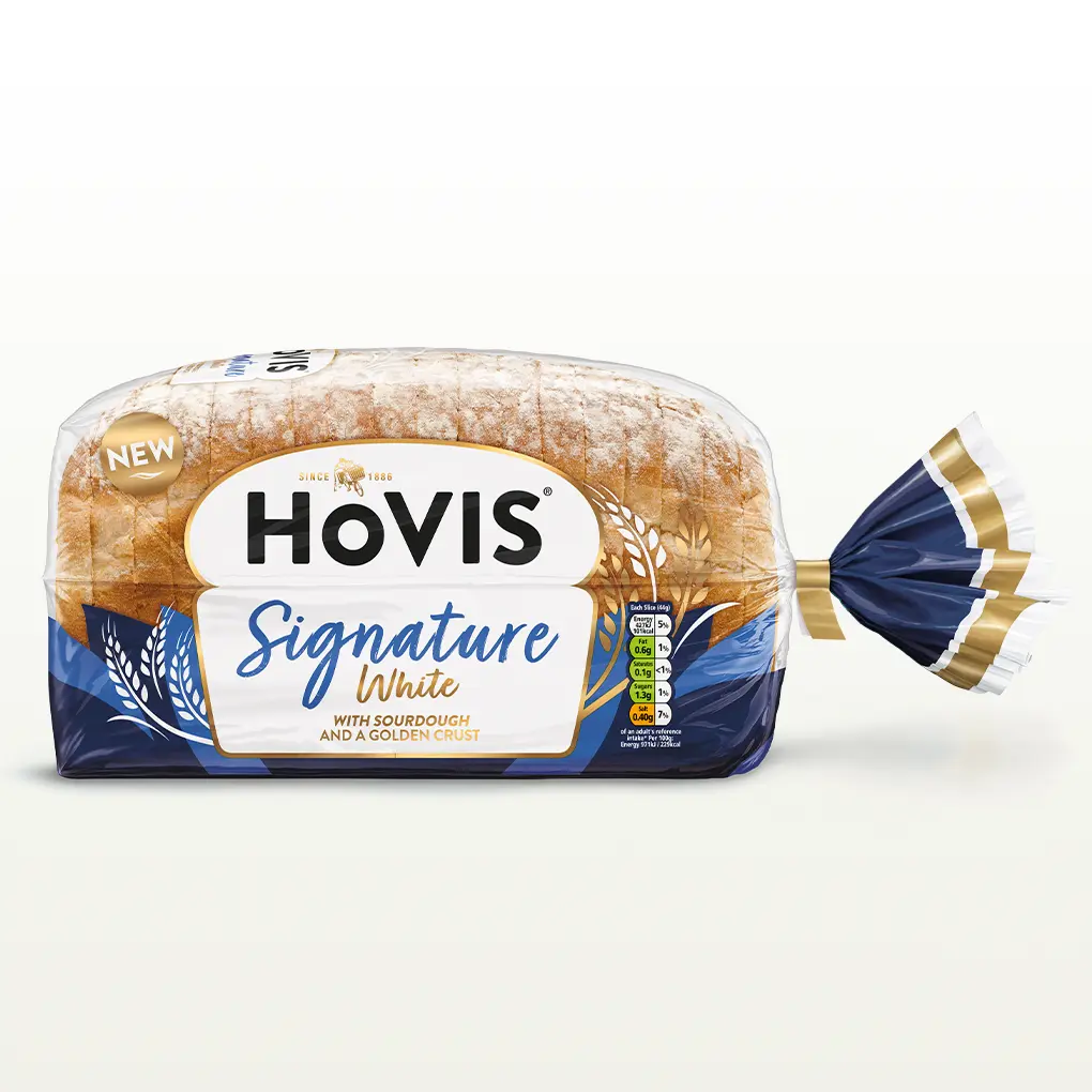 Hovis Signature White bread on a white backdrop with a subtle shadow. The packaging is half transparent and with tones of blue, decorated with wheats.