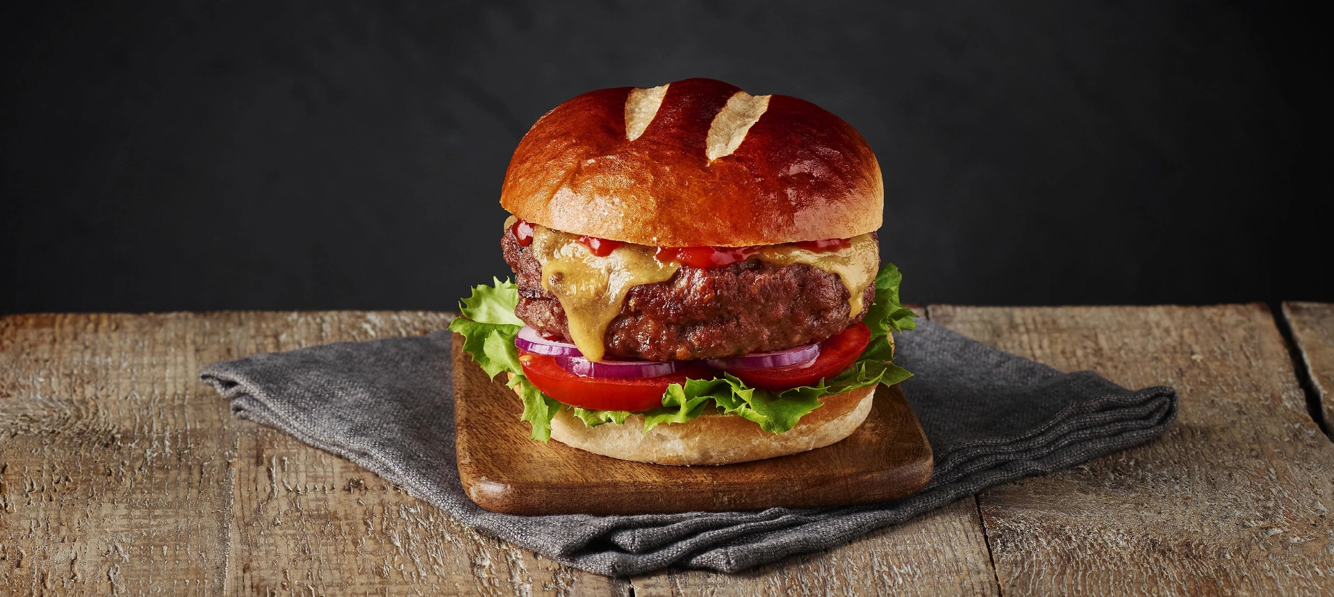 A burger made with Hovis Burger Buns, filled with a meat patty, molten cheese, sliced red onions, tomatoes, and lettuce leaves.