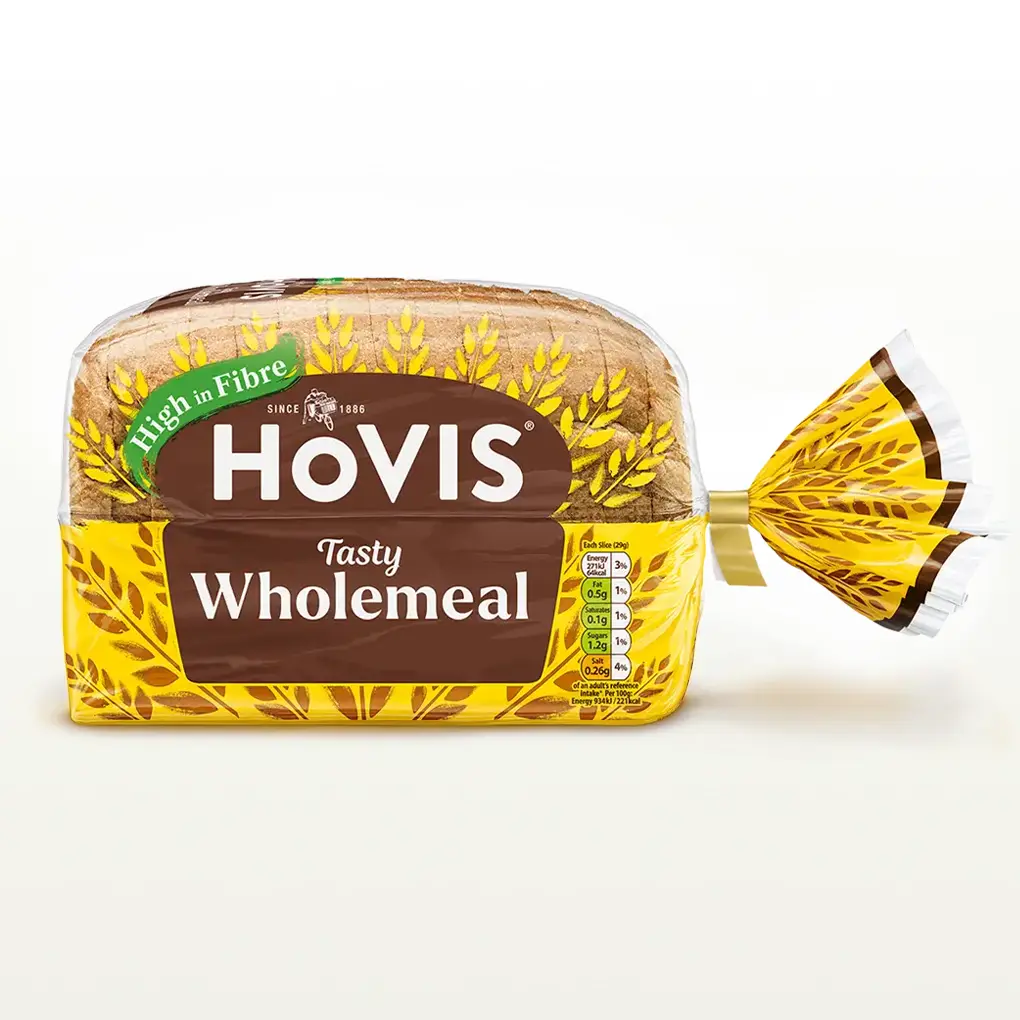 Hovis Tasty Wholemeal 400g bread on a white backdrop with a subtle shadow. The packaging is half transparent and half yellow, decorated with golden wheats.