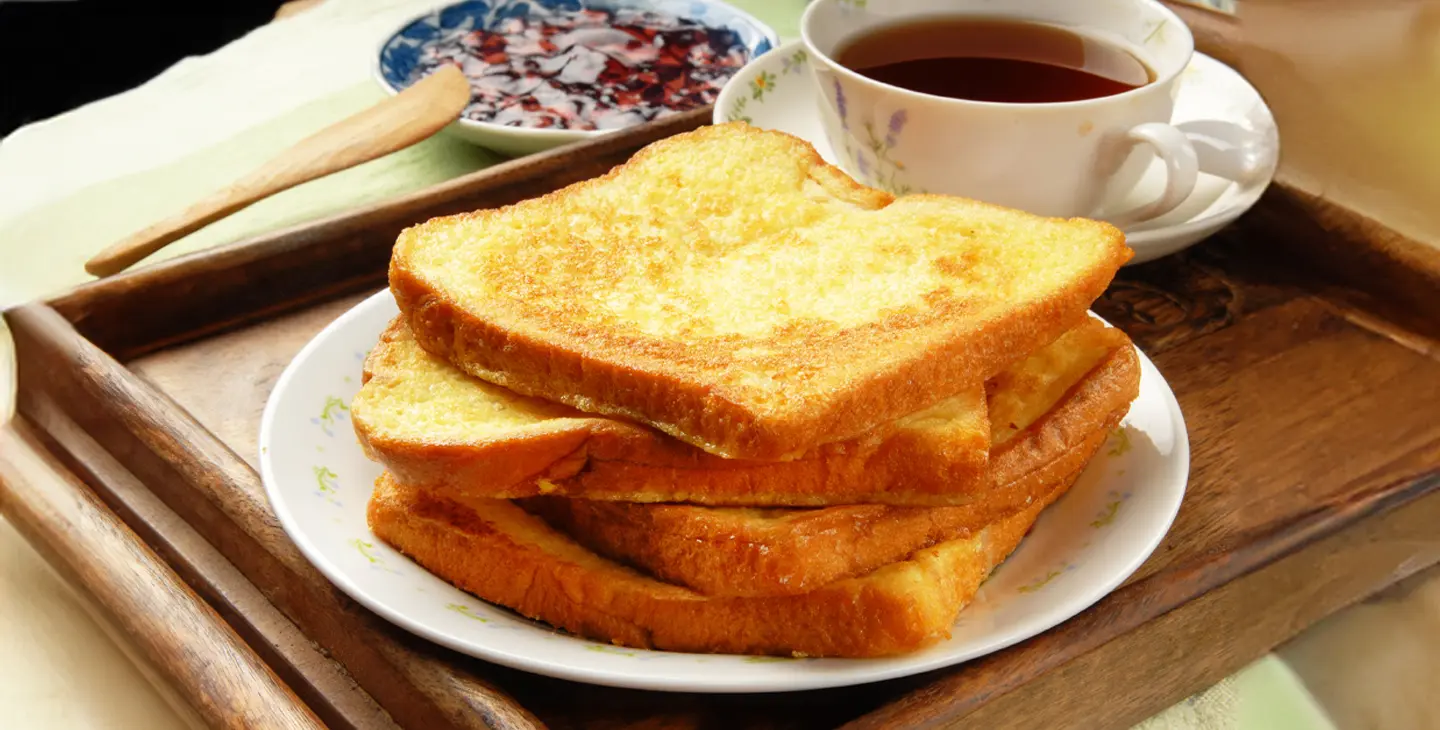 A plate of egg bread stacked on top of each sits on a place with a cup of tea nearby.
